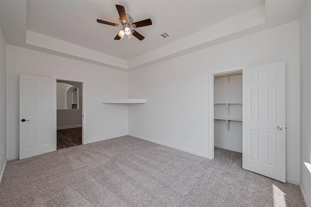 unfurnished bedroom with baseboards, carpet floors, a walk in closet, visible vents, and a tray ceiling