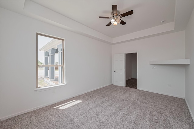 carpeted empty room with visible vents, ceiling fan, a raised ceiling, and baseboards