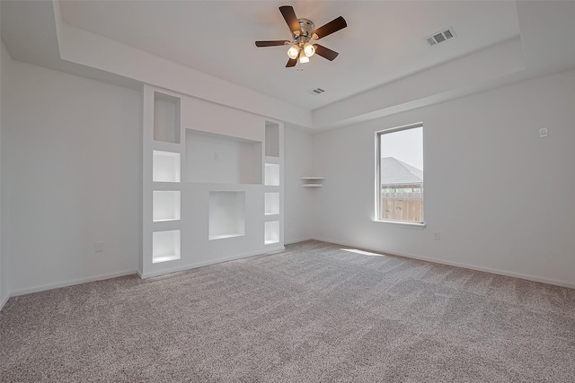 unfurnished bedroom with a tray ceiling, carpet flooring, visible vents, and baseboards