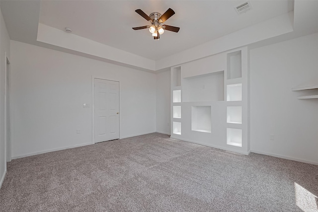 empty room featuring built in features, a ceiling fan, visible vents, carpet flooring, and baseboards