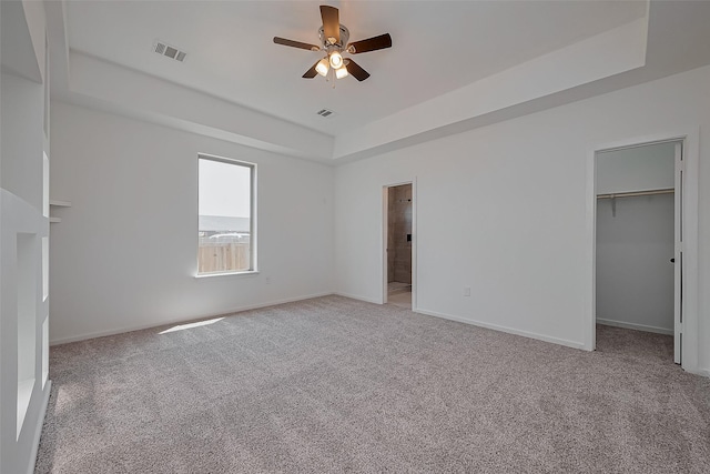 unfurnished bedroom with visible vents, baseboards, a spacious closet, a tray ceiling, and light colored carpet