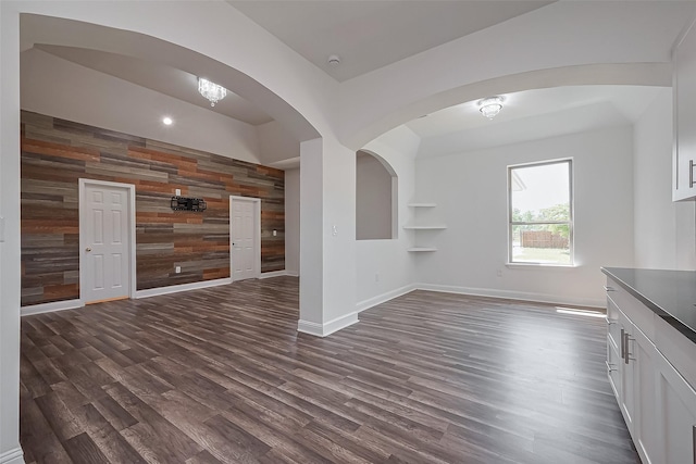 unfurnished living room featuring dark wood-type flooring, wood walls, and baseboards