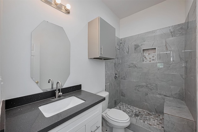 bathroom with toilet, tiled shower, and vanity