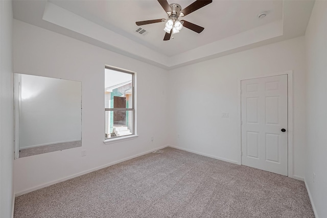 unfurnished room featuring a raised ceiling, carpet flooring, ceiling fan, and visible vents