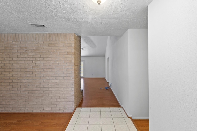 corridor featuring a textured ceiling, brick wall, wood finished floors, visible vents, and baseboards