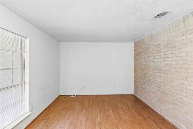 empty room featuring brick wall, visible vents, a textured ceiling, and light wood finished floors