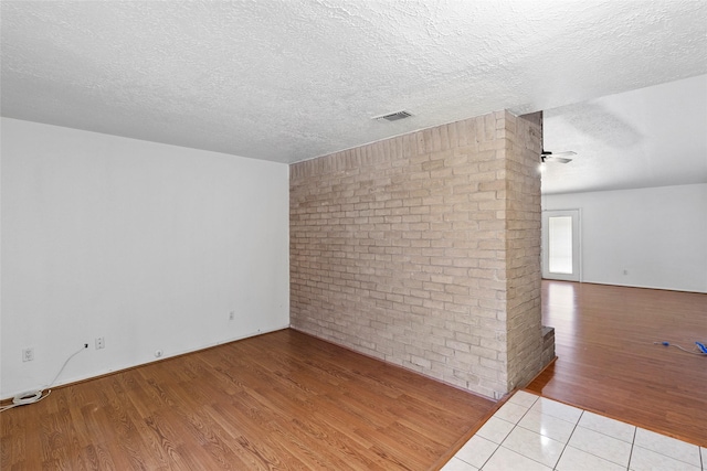 empty room with a ceiling fan, a textured ceiling, visible vents, and wood finished floors