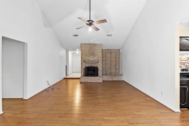 unfurnished living room with ceiling fan, high vaulted ceiling, visible vents, light wood-style floors, and a brick fireplace