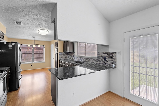 kitchen featuring visible vents, decorative backsplash, a peninsula, light wood-type flooring, and a sink