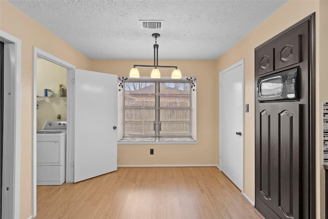 unfurnished dining area with washer / clothes dryer, visible vents, a textured ceiling, and light wood finished floors