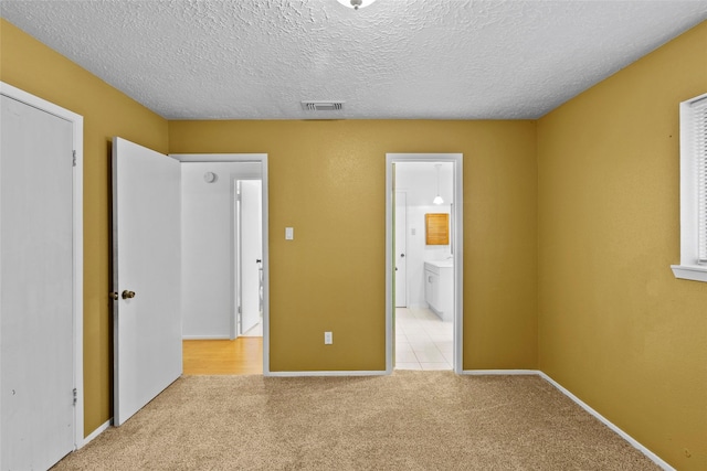 unfurnished bedroom with light carpet, a textured ceiling, visible vents, and connected bathroom