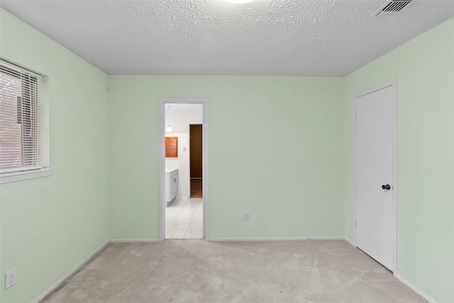 spare room featuring a textured ceiling, baseboards, visible vents, and light colored carpet