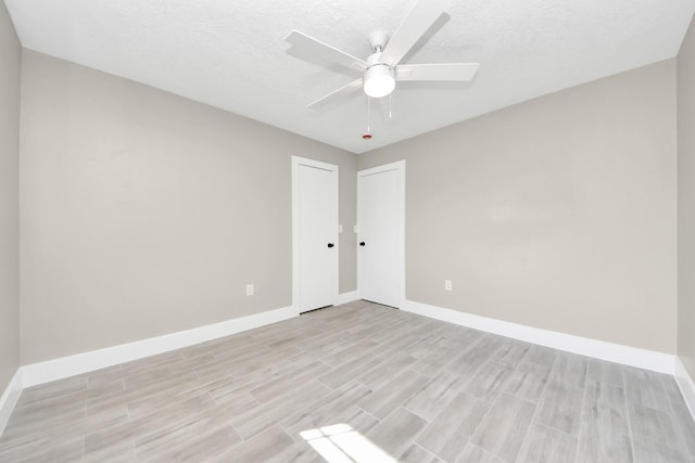 empty room featuring light wood-type flooring, a textured ceiling, baseboards, and a ceiling fan