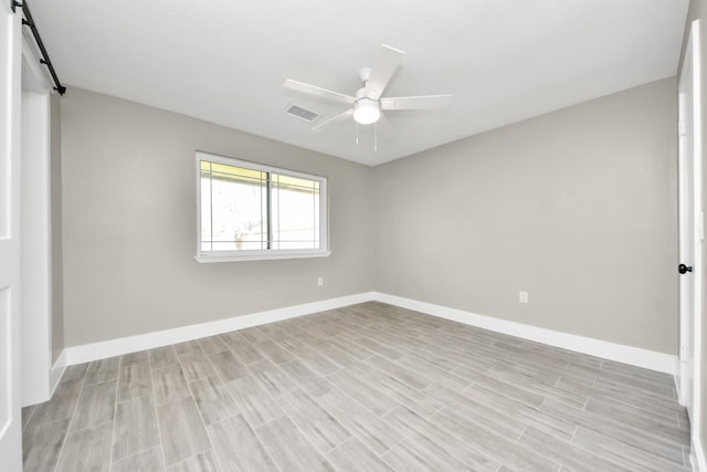 unfurnished room with a barn door, visible vents, ceiling fan, and baseboards