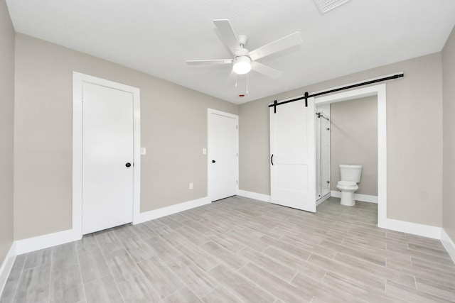 unfurnished bedroom featuring a barn door, visible vents, baseboards, and wood finish floors