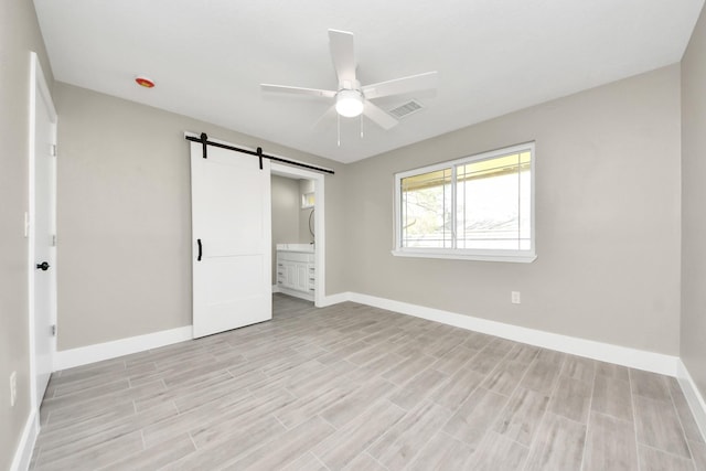 unfurnished bedroom featuring a barn door, visible vents, baseboards, ensuite bath, and light wood-type flooring