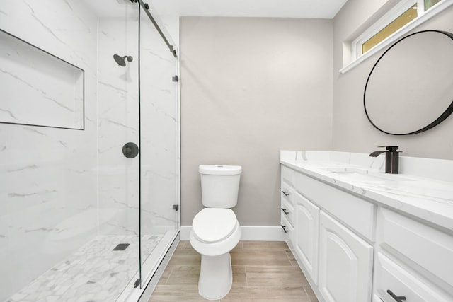 full bath with toilet, wood finish floors, vanity, baseboards, and a marble finish shower