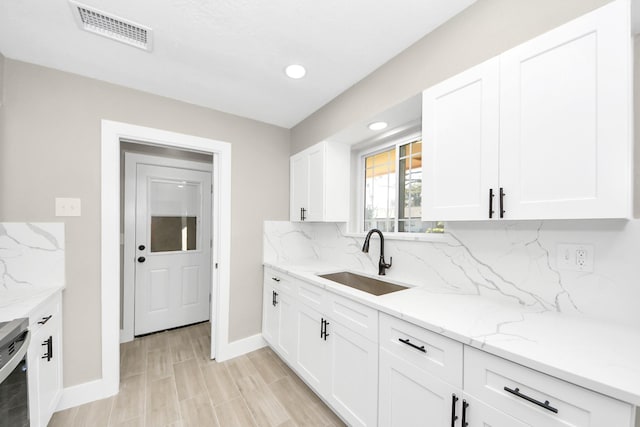 kitchen featuring tasteful backsplash, visible vents, a sink, and white cabinetry