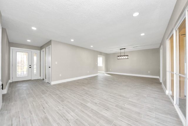 interior space featuring a textured ceiling, recessed lighting, light wood-type flooring, and baseboards