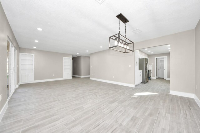 unfurnished dining area with a textured ceiling, light wood-type flooring, and baseboards