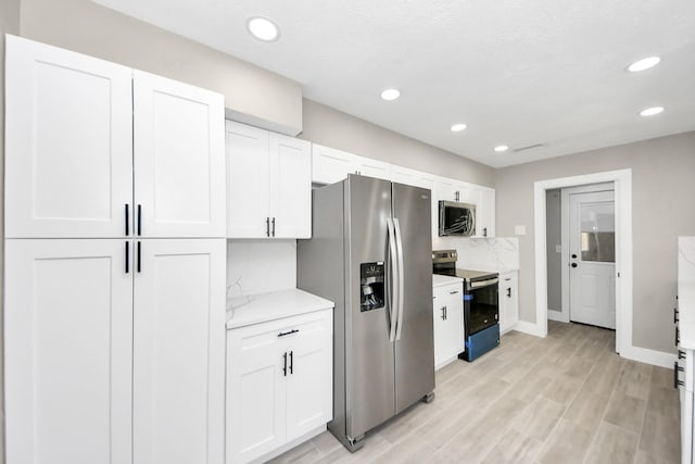 kitchen with stainless steel appliances, recessed lighting, white cabinetry, and light stone countertops