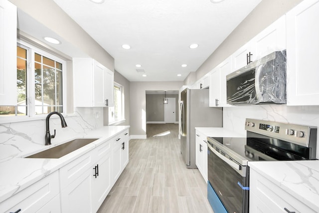 kitchen featuring light stone countertops, a sink, white cabinets, appliances with stainless steel finishes, and decorative backsplash