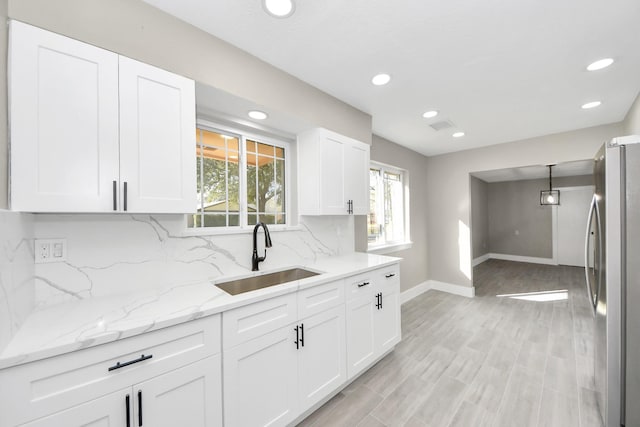 kitchen featuring pendant lighting, tasteful backsplash, freestanding refrigerator, white cabinets, and a sink