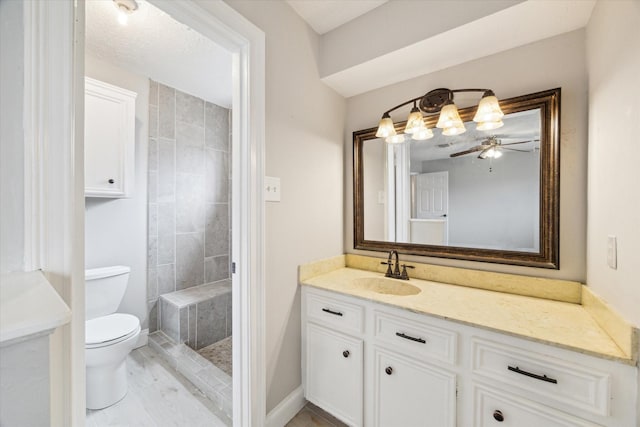 full bathroom with toilet, baseboards, a tile shower, and vanity