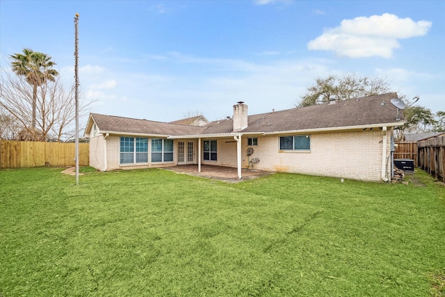 rear view of property featuring a patio area, a fenced backyard, a chimney, and a yard