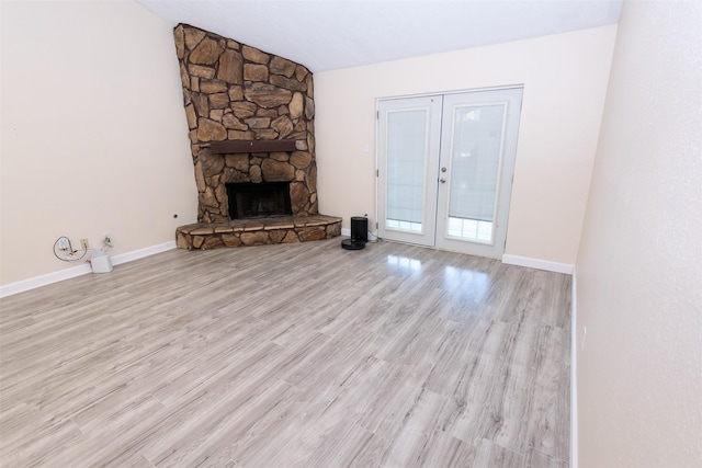 unfurnished living room featuring a stone fireplace, wood finished floors, baseboards, vaulted ceiling, and french doors