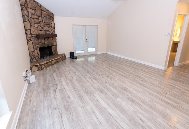 unfurnished living room featuring french doors, vaulted ceiling, a stone fireplace, wood finished floors, and baseboards