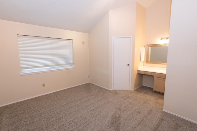 unfurnished bedroom with lofted ceiling, ensuite bathroom, light carpet, baseboards, and built in desk