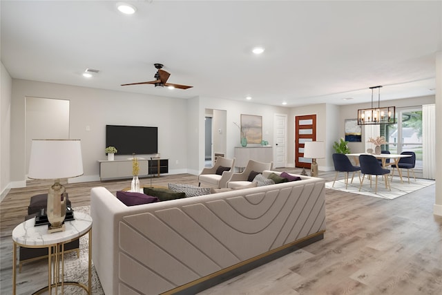 living room with light wood-type flooring, ceiling fan with notable chandelier, baseboards, and recessed lighting