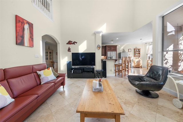 living room featuring a towering ceiling, baseboards, arched walkways, and light tile patterned flooring