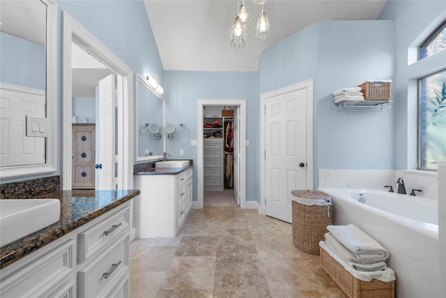 bathroom with a garden tub, a spacious closet, two vanities, and a sink