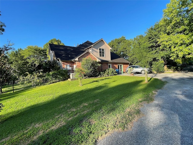 view of side of home featuring a yard, gravel driveway, brick siding, and fence