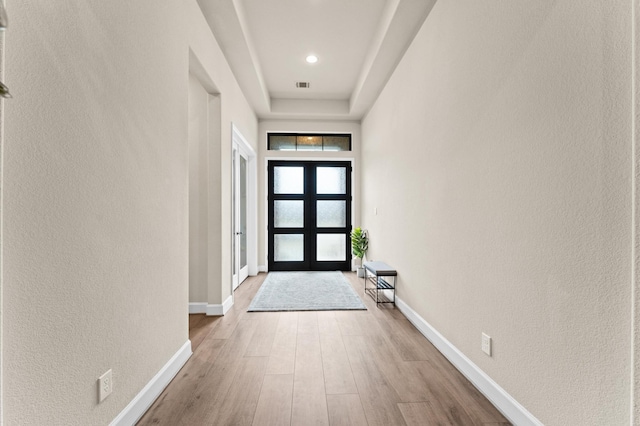 entryway featuring light wood-style floors, french doors, a textured wall, and baseboards