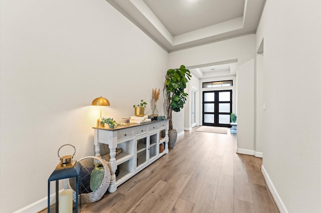 entrance foyer featuring light wood-style floors, baseboards, a tray ceiling, and french doors