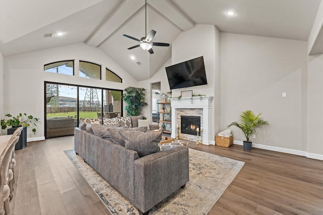 living room with high vaulted ceiling, a stone fireplace, wood finished floors, and beam ceiling