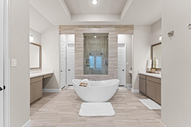 full bath with vanity, baseboards, a freestanding bath, a shower stall, and a raised ceiling