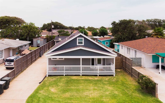 rear view of property featuring covered porch, a lawn, fence, and a residential view