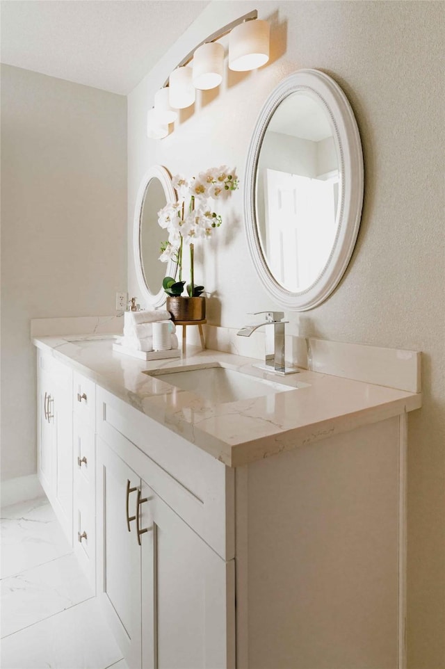 bathroom with marble finish floor, double vanity, a sink, and baseboards