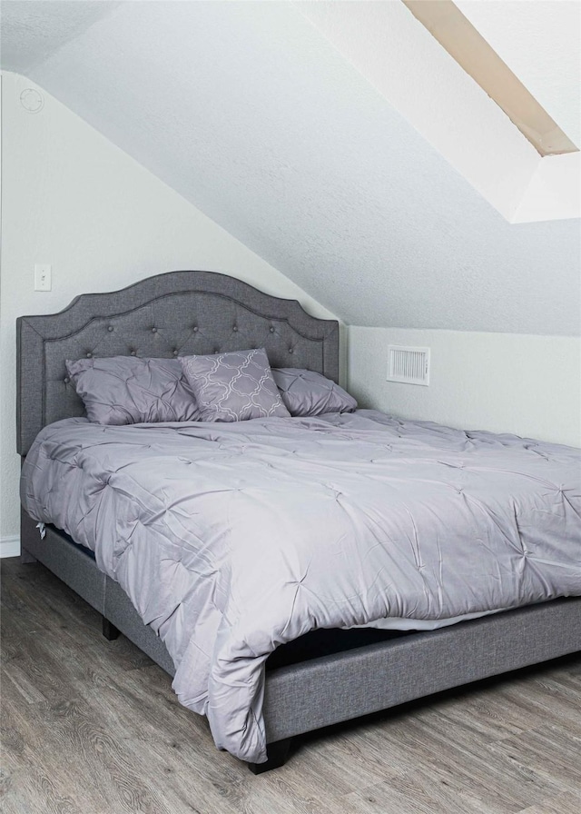 bedroom with visible vents, vaulted ceiling, and wood finished floors