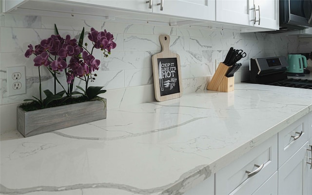 room details featuring light stone countertops, stainless steel range with electric stovetop, white cabinetry, and decorative backsplash