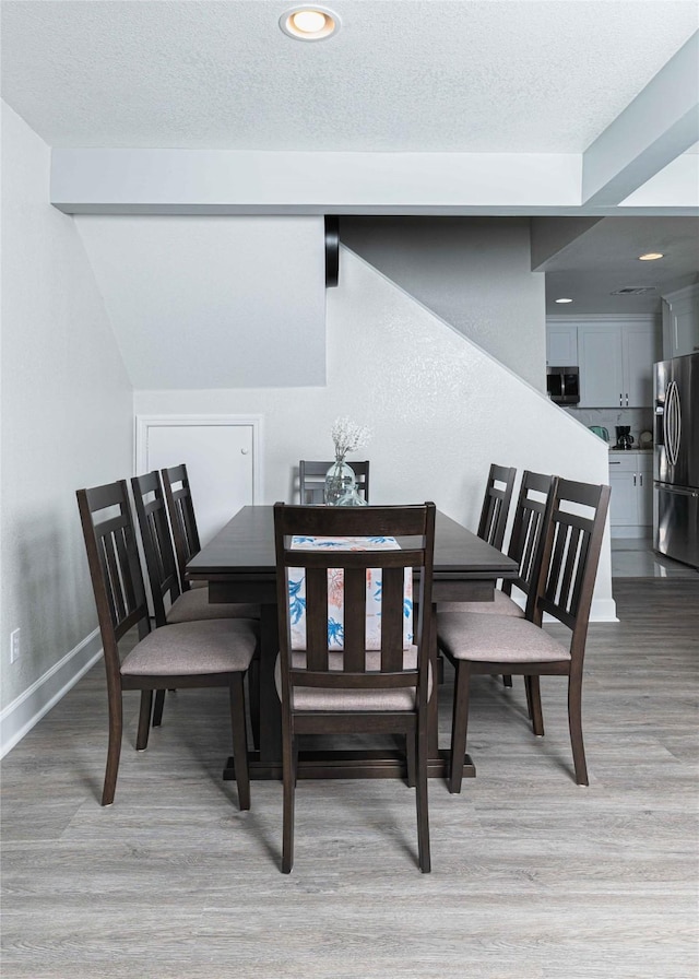 dining space with baseboards, a textured ceiling, and light wood finished floors