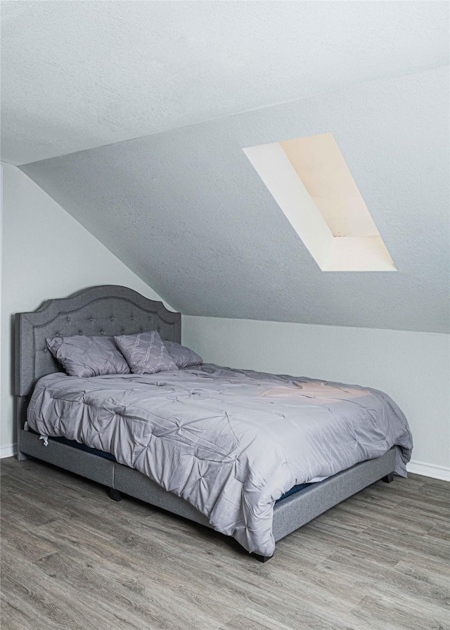 bedroom with vaulted ceiling, a textured ceiling, baseboards, and wood finished floors