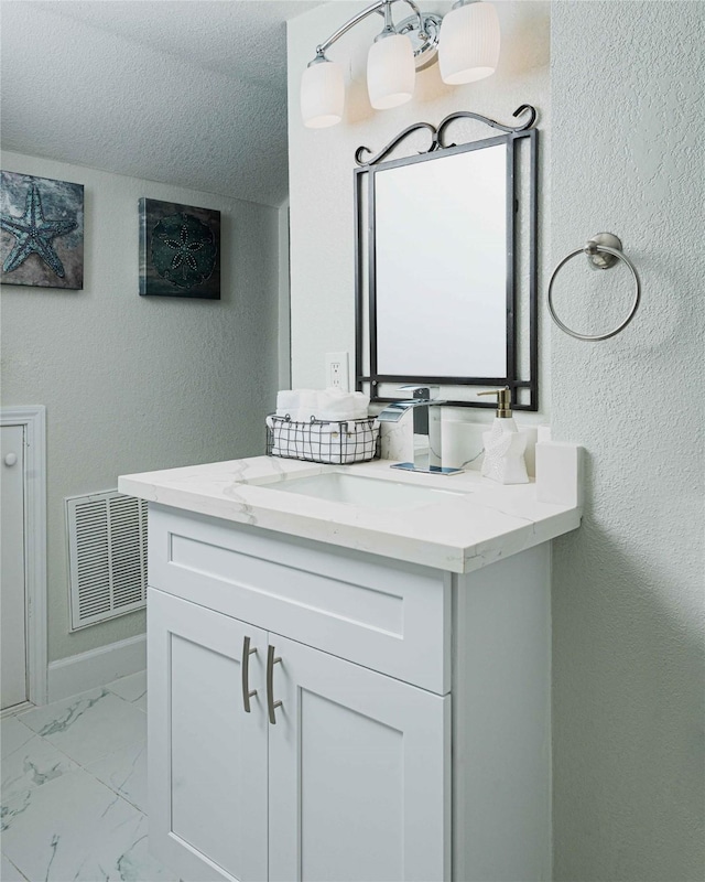 bathroom featuring marble finish floor, visible vents, a textured wall, vanity, and a textured ceiling