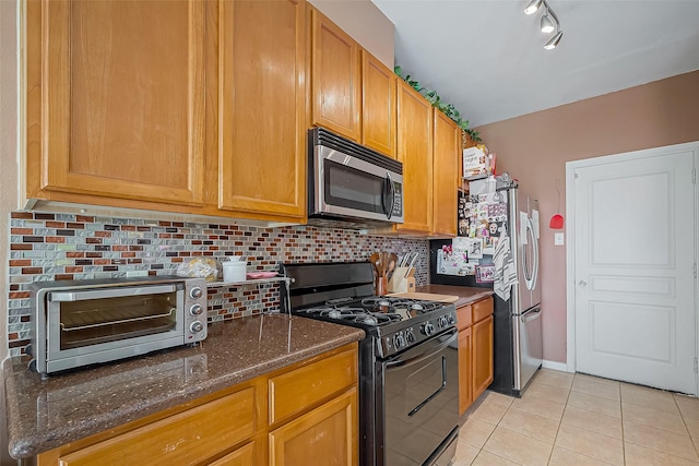 kitchen featuring a toaster, tasteful backsplash, appliances with stainless steel finishes, dark stone countertops, and light tile patterned flooring