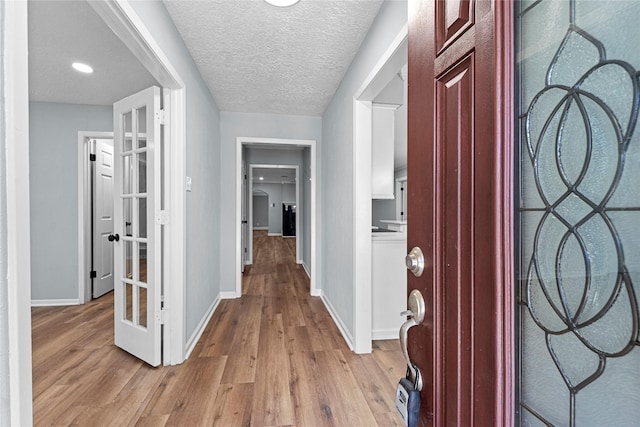 corridor featuring french doors, light wood-style flooring, baseboards, and a textured ceiling