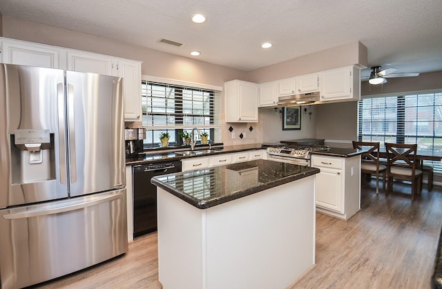 kitchen featuring visible vents, appliances with stainless steel finishes, white cabinets, a kitchen island, and a sink